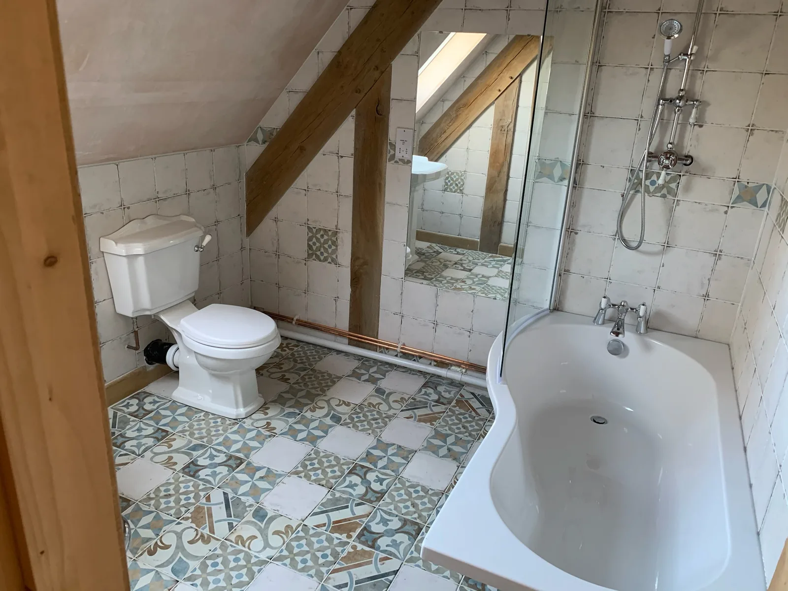 Loft bathroom with sloped ceiling, exposed beams and encaustic floor tiles